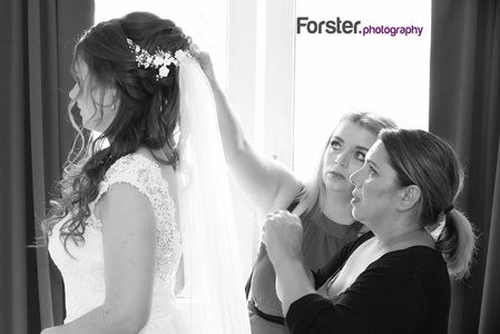 Eine Braut steht vor der Hochzeit beim getting ready Fotoshooting im Wohnzimmer, Trauzeugen helfen beim Schleier