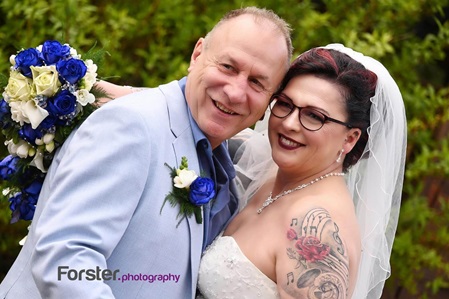 Hochzeitspaar im schönen Outfit und mit Brautstrauß schaut verliebt in die Kamera beim Brautpaar-Fotoshooting