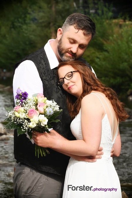 Brautpaar umarmt sich am Hochzeitstag sehr innig mit geschlossenen Augen. Die Braut hat ihren Strauß in der Hand.