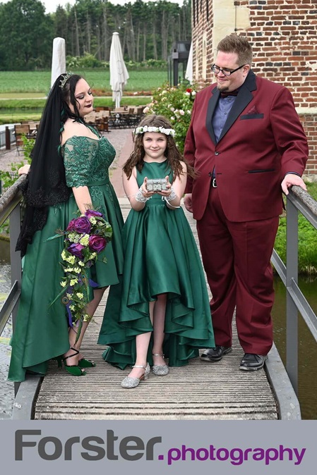 Elegantes Brautpaar beim Fotoshooting auf der Brücke vor dem Schloss. Brautjungfer im grünen Kleid zeigt die Ringe