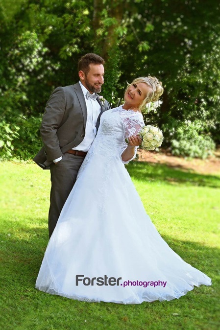 Ein Hochzeitspaar steht beim Fotoshooting auf einer Wiese. Die Braut blickt glücklich in die Kamera