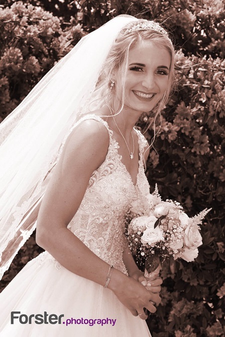 Eine elegante Braut im weißen Hochzeitskleid lächelt beim Fotoshooting glücklich in die Kamera