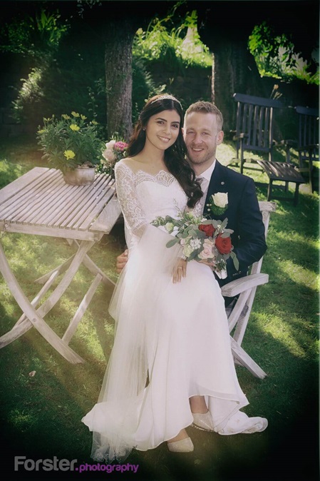 Ein Brautpaar sitzt beim Fotoshooting nach der Hochzeit in einem Garten und blickt glücklich in die Kamera