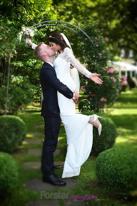 Ein Brautpaar steht beim Fotoshooting nach der Hochzeit in einem Garten. Der Bräutigam hebt die Braut in die Luft