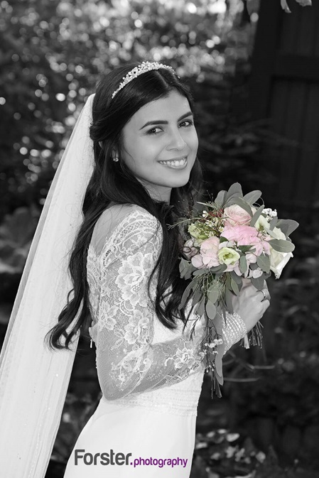 Eine Braut im weißen Hochzeitskleid mit Schleier und Brautstrauß lächelt beim Fotoshooting glücklich in die Kamera