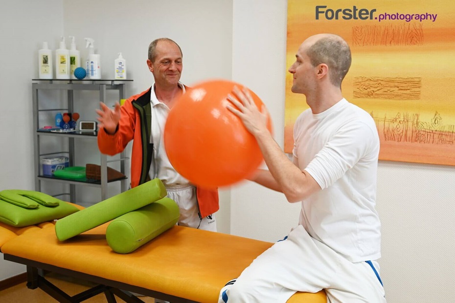 Zwei Physiotherapeuten werfen sich einen Gymnastikball lächelnd zu
